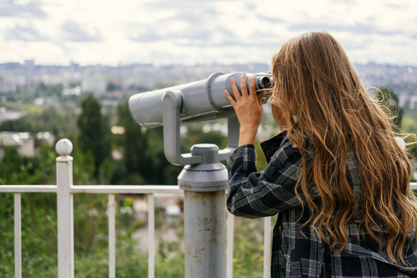 Back shot of a blonde woman looking to the city through some big sight seeing binoculars. - Foto, Imagem
