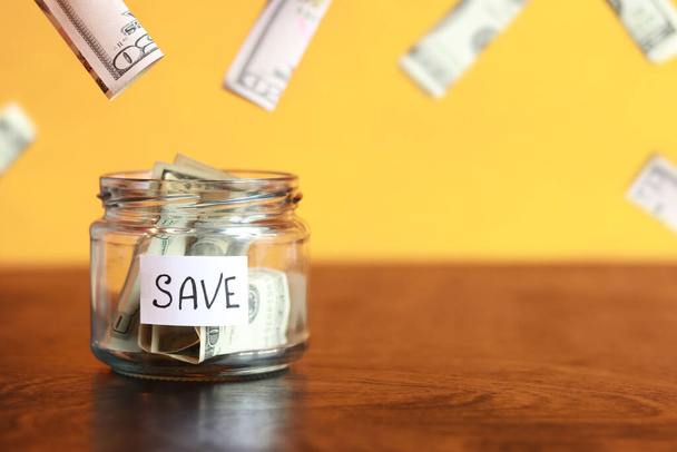 Save money for the future. Glass jar with dollars on a wooden table. Piggy bank with banknotes and dollars flying around. copy space. The concept of financial savings - Photo, Image