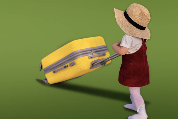 Una piccola ragazza carina gioiosa in un abito estivo blu e un cappello di paglia tiene una valigia gialla. Vacanze, vacanze, gita al mare, spazio per testo, andare in vacanza - Foto, immagini