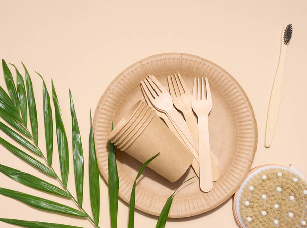 Paper plates, wooden forks and a toothbrush on a beige background, top view. Concept of recyclable garbage, zero waste - Photo, Image