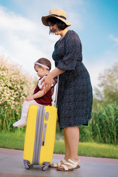 Ταξιδιωτική ιδέα: η μαμά και η κόρη με μια βαλίτσα ετοιμάζονται για ένα ταξίδι, ένα παιδί κάθεται σε μια βαλίτσα, μια μητέρα τυλίγει ένα παιδί σε μια βαλίτσα, διακοπές στη θάλασσα, ταξίδια με την οικογένεια - Φωτογραφία, εικόνα