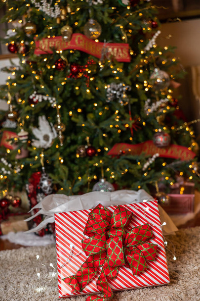 Christmas tree with lights and ornaments and a beautifully wrapped present underneath with a large bow. - Photo, Image