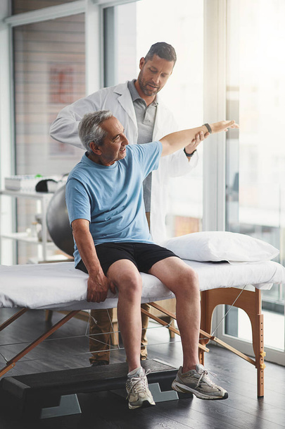 Unter seiner Führung wird die Erholung schnell vonstatten gehen. ein junger männlicher Physiotherapeut hilft einem älteren Patienten bei der Genesung - Foto, Bild