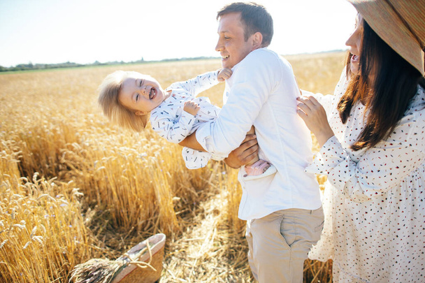 Happy family on a summer walk, mother, father and child walk in the wheat field and enjoy the beautiful nature, at sunset. High quality photo - 写真・画像