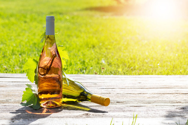 Белые и розовые бутылки вина на открытом столе сад, устанавливая сцену для восхитительной летней вечеринки. С копировальным местом - Фото, изображение