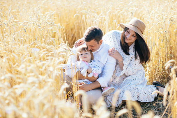 Feliz infancia, familia caminando en el campo de trigo. Madre, padre e hija pequeña descansan juntos al aire libre. Padres y niños jugando en el prado de verano. Foto de alta calidad - Foto, Imagen