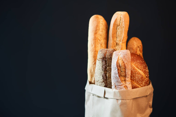 Different types of french bread baguettes in paper bag over dark background with copy space. Bakery, delicious food concept - Фото, зображення