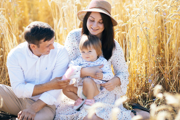 Happy childhood, family walking on the wheat field. Mother, father and little daughter leisures together outdoor. Parents and kid playing on summer meadow. High quality photo - Photo, Image