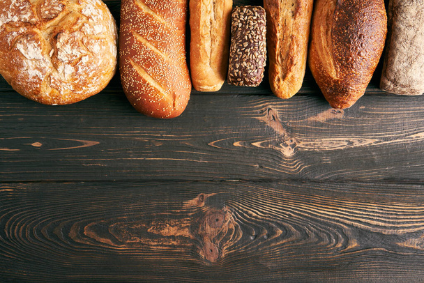 Different types of bread loaves on wooden background with copy space. Bakery, delicious food concept. Top view - Foto, immagini