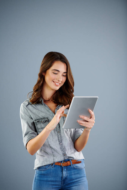 Jej blog naprawdę zaczyna się układać. Studyjne ujęcie atrakcyjnej młodej kobiety używającej tabletu cyfrowego na szarym tle - Zdjęcie, obraz
