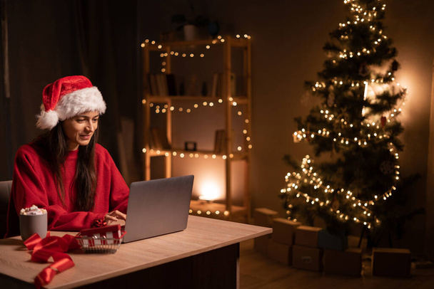 Christmas sales concept. Woman typing on laptop in home interior in the evening. Planning holidays. Web search. Copy space - Фото, изображение