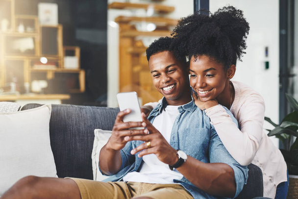 Look at this one babe. a happy young couple using a mobile phone together on the sofa at home - Foto, Bild