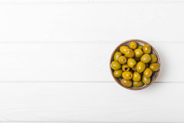Zelené olivy na bílém dřevěném pozadí. Různé druhy oliv v miskách a olivovém oleji s čerstvými olivovými listy. Rozumím. Místo pro text. Středomořské jídlo. Vegan. - Fotografie, Obrázek