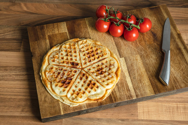 Pizza waffle with pepperoni, olives and parmesan cheese and cherry tomatoes on a cutting board on the kitchen table - Photo, Image