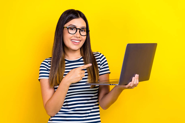 Photo of young cheerful programmer chinese woman pointing finger her new hp netbook modern gadget isolated on yellow color background. - Fotoğraf, Görsel