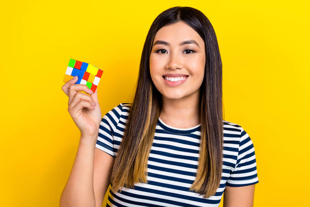 Photo of optimistic funny young chinese woman wear sailor t-shirt hold rubik cube playing logic toy isolated on yellow color background. - Foto, Imagen