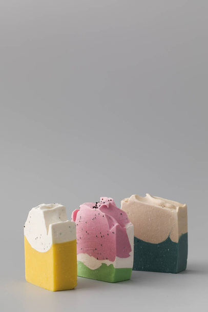 Pieces of different shapes and colors of handmade soap on a grey background. The concept of natural cosmetics, hygiene. Copy space - 写真・画像