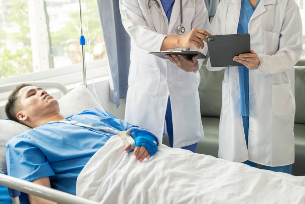 Two doctors talking to a patient lying in bed while receiving saline solution in hospital Professional medical service concept Attentive doctor comforting a patient Stock Picture - Foto, imagen