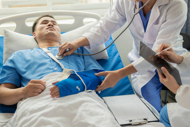 Dwóch lekarzy rozmawiających z pacjentem leżącym w łóżku, otrzymującym roztwór soli fizjologicznej w szpitalu Koncepcja profesjonalnej opieki medycznej Uwaga lekarz pocieszający pacjenta Zdjęcie Stockowe - Zdjęcie, obraz