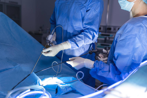 Chirurgen team kijkt naar monitoren tijdens preforming operatie in het ziekenhuis operatiekamer, mannelijke chirurg opererende patiënt werken met chirurgische laparoscopie instrumenten. - Foto, afbeelding