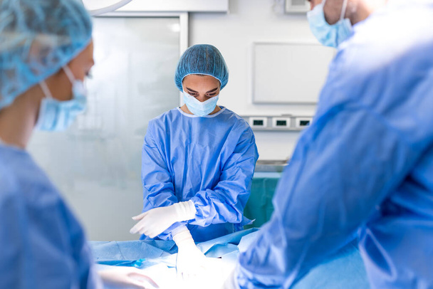 Zespół profesjonalnych chirurgów, asystentów i pielęgniarek wykonujących operacje inwazyjne na pacjencie w sali operacyjnej szpitala. Chirurdzy rozmawiają i używają instrumentów. Prawdziwy nowoczesny szpital. - Zdjęcie, obraz