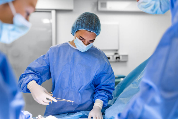 Medical team performing operation. Group of surgeon at work in operating theatre toned in blue. Doctor operation in operation room at hospital concept for insurance advertising. - Valokuva, kuva