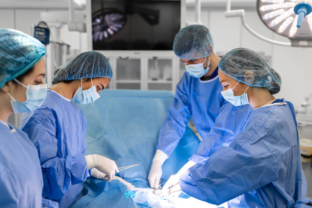 Szakmai sebészek, asszisztensek és nővérek csapata, akik invazív műtétet végeznek egy betegen a kórház műtőjében. A sebészek beszélnek és hangszereket használnak. Igazi modern kórház.. - Fotó, kép