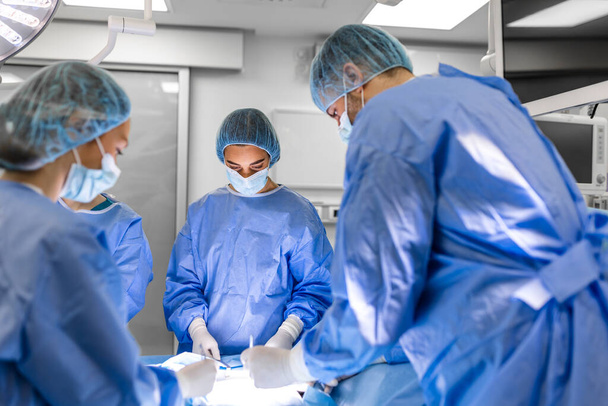 Group of medical team urgently doing surgical operation and helping patient in theater at hospital. Medical team performing surgical operation in a bright modern operating room - Photo, image