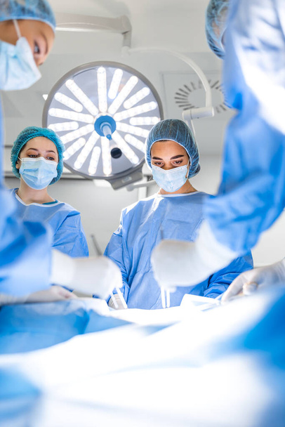 Preparation for the beginning of surgical operation with a cut. Group of surgeons at work in operating theater toned in blue. Medical team performing operation - Fotoğraf, Görsel