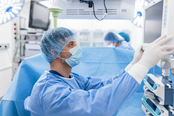 Anestezjolog śledzący funkcje życiowe organizmu podczas operacji serca. Chirurg patrzy na monitor medyczny podczas operacji. Kontrola stanu zdrowia pacjenta przez lekarza. - Zdjęcie, obraz