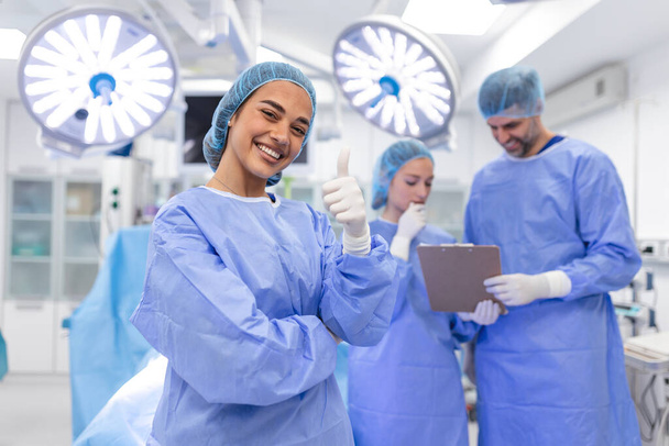 Portrait of female woman nurse surgeon OR staff member dressed in surgical scrubs gown mask and hair net in hospital operating room theater making eye contact smiling pleased happy looking at camera - Foto, imagen