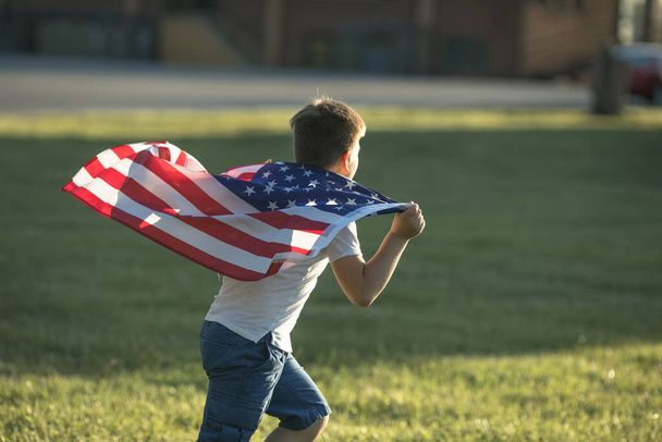Chłopiec świętujący 4 lipca Dzień Niepodległości USA. Dziecko biegające z amerykańskim symbolem flagi Stanów Zjednoczonych na polu pszenicy. - Zdjęcie, obraz