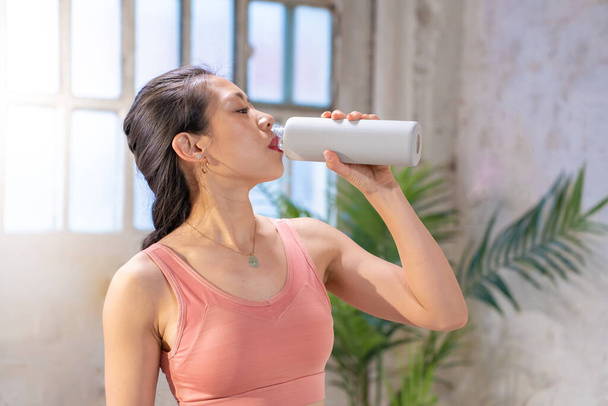 Mooie sportieve Aziatische vrouw die water drinkt uit een kantine. Gezond levensstijl concept. Hoge kwaliteit foto - Foto, afbeelding