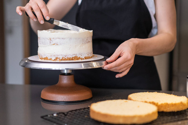 Food blogger confectioner preparar delicioso bolo livre de lactose para o evento em casa mulher em avental preto em pé na mesa da cozinha demonstra manchas creme branco em confeitaria artesanal - Foto, Imagem