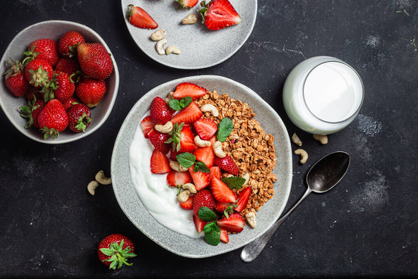 Granola with yogurt and strawberries in a plate on a dark background - Photo, Image