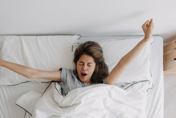 Top view of yawning and stretching asian woman just wake up on the bed. - Фото, изображение