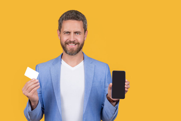 ecommerce concept. happy man paying online, ecommerce. man paying online hold phone and ecommerce card with copy space. man paying ecommerce online isolated on yellow. man paying online in studio. - Photo, Image