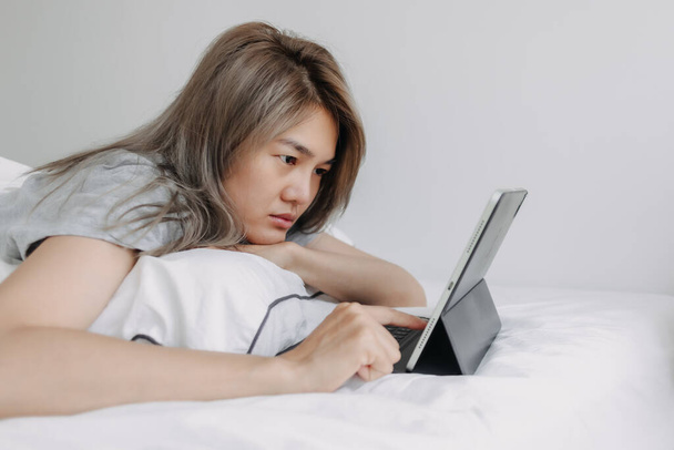 Asian woman working online on the tablet computer on the bed in the morning. - 写真・画像