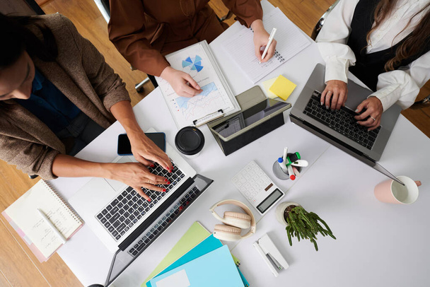 Vista superior de las empresarias que trabajan en computadoras y examinan las cartas financieras en equipo mientras están sentadas en la mesa - Foto, imagen