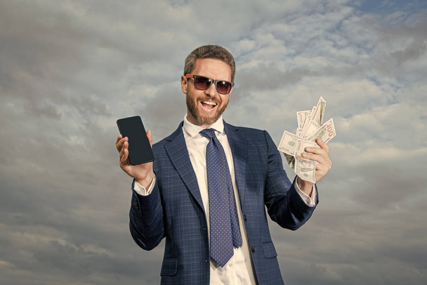 cheerful betting man with lottery money outdoor. betting man with lottery money hold phone. photo of betting man with lottery money. betting man with lottery money on sky background. - Foto, Imagen