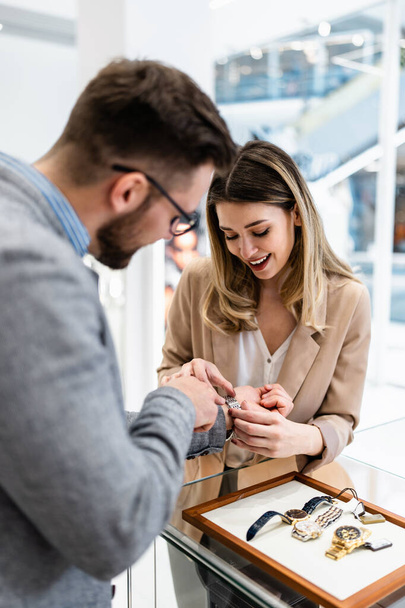 Elegant middle age businessman choosing and buying his new expensive watch. Beautiful young female seller helps him to make good decision. Fashion style and elegance concept. - Photo, image