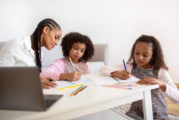 E-Learning. Dvě černé školačky učení na notebooku, mají lekce s lektorem v útulný domácí interiér. Matka pomáhá svým dětem s dálkovým studiem a domácím úkolem rutiny. Koncepce domácího školství - Fotografie, Obrázek