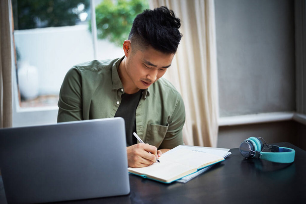 Робота відповідно до стислого дизайну. красивий молодий чоловік робить нотатки під час роботи на ноутбуці вдома
 - Фото, зображення