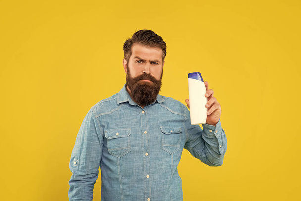 brutal bearded man hold shampoo bottle on yellow background, haircare. - Foto, imagen