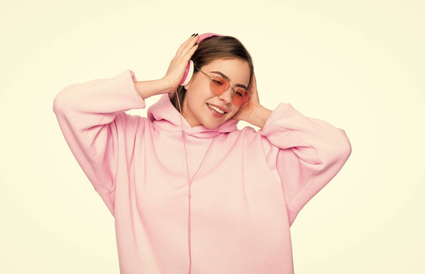 Happy young woman in pink hoodie and glasses enjoy listening to music in headphones isolated on white. - Фото, зображення