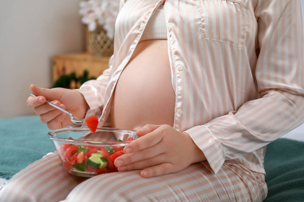 Young pregnant woman eating vegetable salad in bedroom, closeup - Fotó, kép