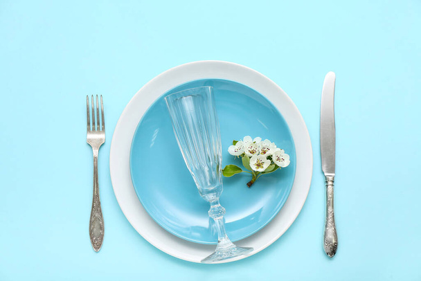 Beautiful table setting with empty glass and blooming tree branch on turquoise background - Foto, afbeelding