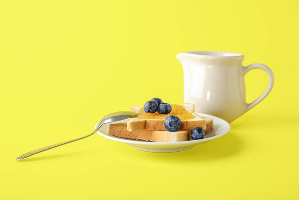 Πιάτο από νόστιμες προπόσεις με μαρμελάδα ροδάκινο, μύρτιλο και γάλα σε κανάτα σε κίτρινο φόντο - Φωτογραφία, εικόνα