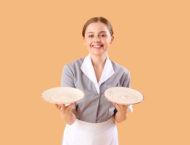 Hermosa joven camarera con platos vacíos sobre fondo beige - Foto, Imagen