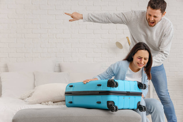 Vihainen aviomies potkii vaimoaan matkalaukku makuuhuoneessa. Perheväkivallan käsite - Valokuva, kuva